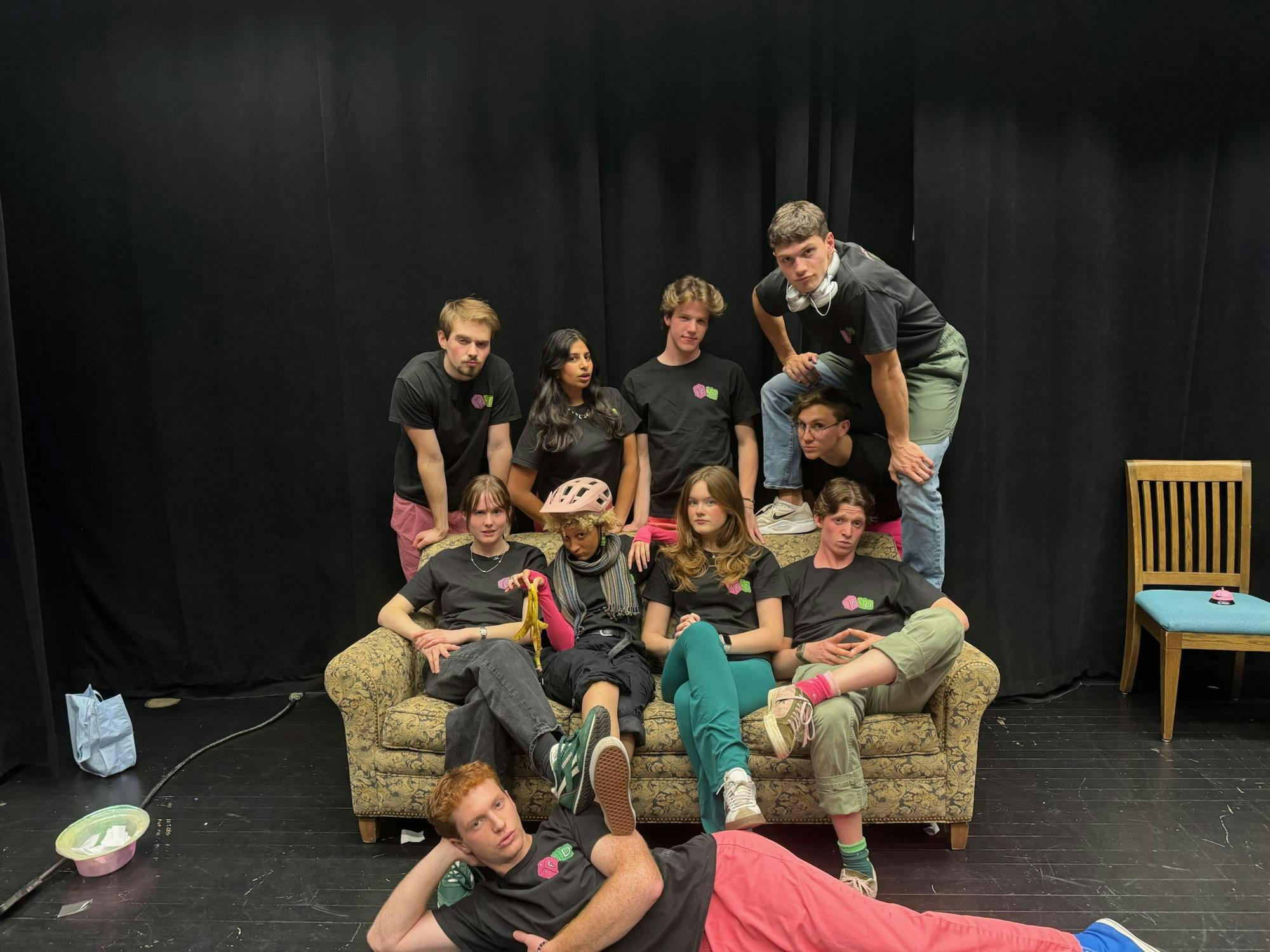 Members of Fuzzy Dice pose for a group picture around a sofa, in matching black t-shirts. 