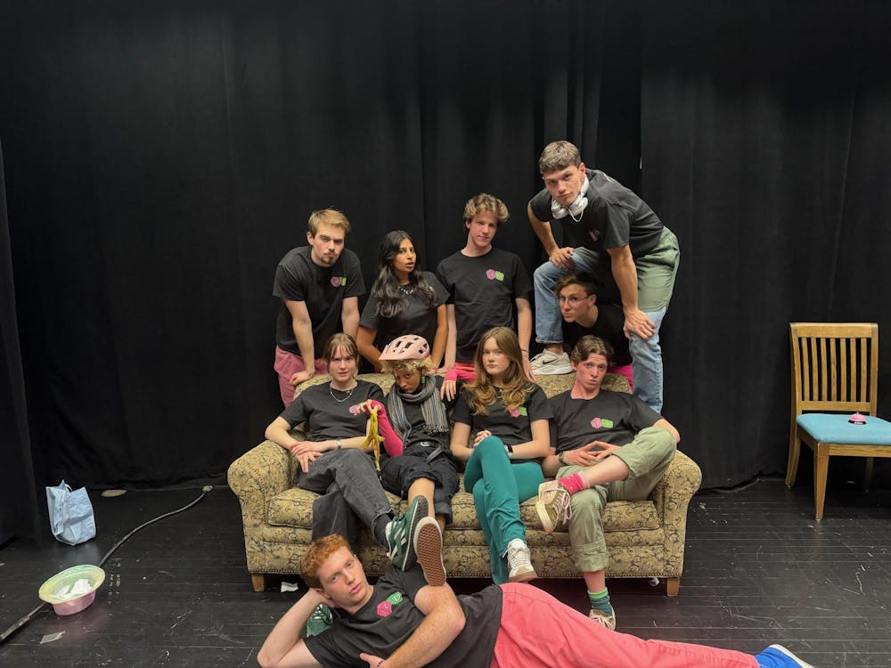 Members of Fuzzy Dice pose for a group picture around a sofa, in matching black t-shirts. 
