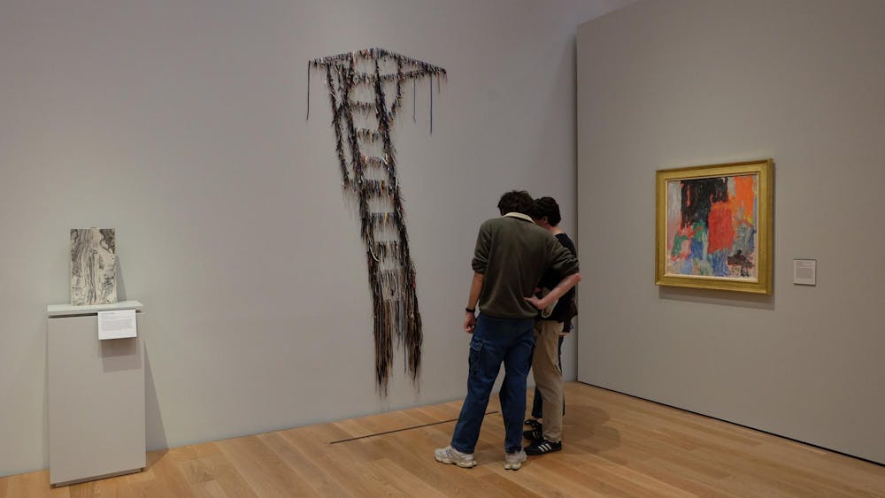 Two people stand in front of an art piece resembling a ladder made of strings. 