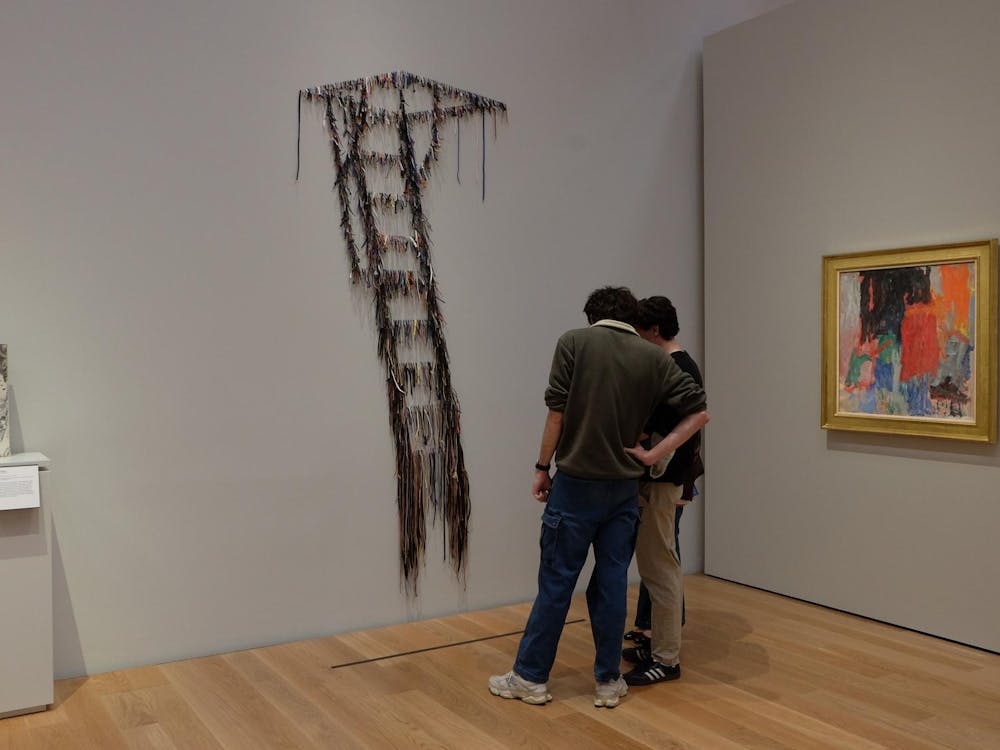 Two people stand in front of an art piece resembling a ladder made of strings.