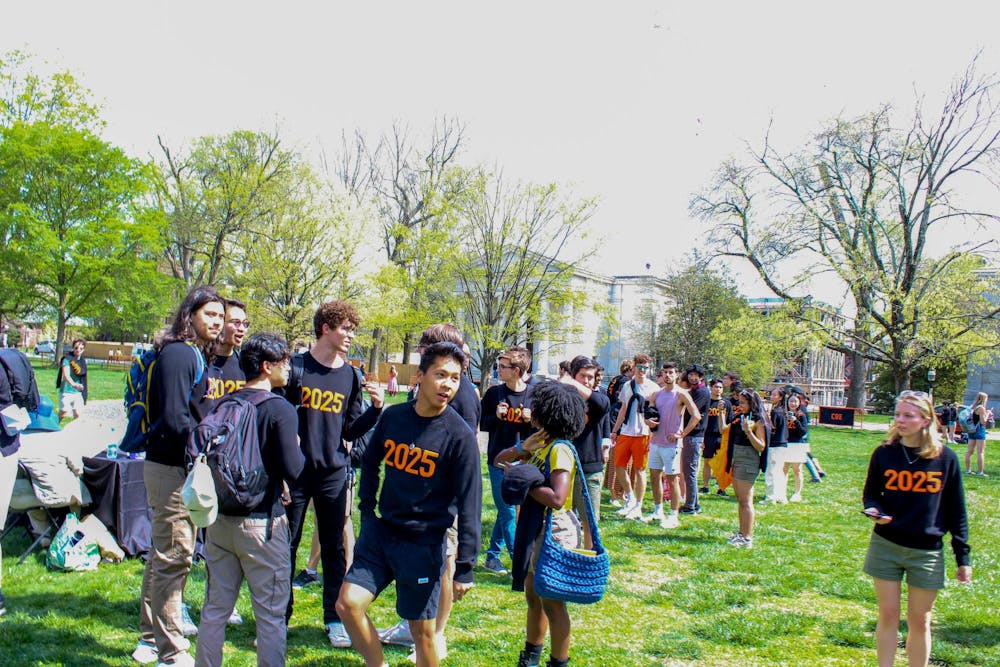 Group of students wearing black sweaters with "2025" written across the front in orange while on a green lawn.