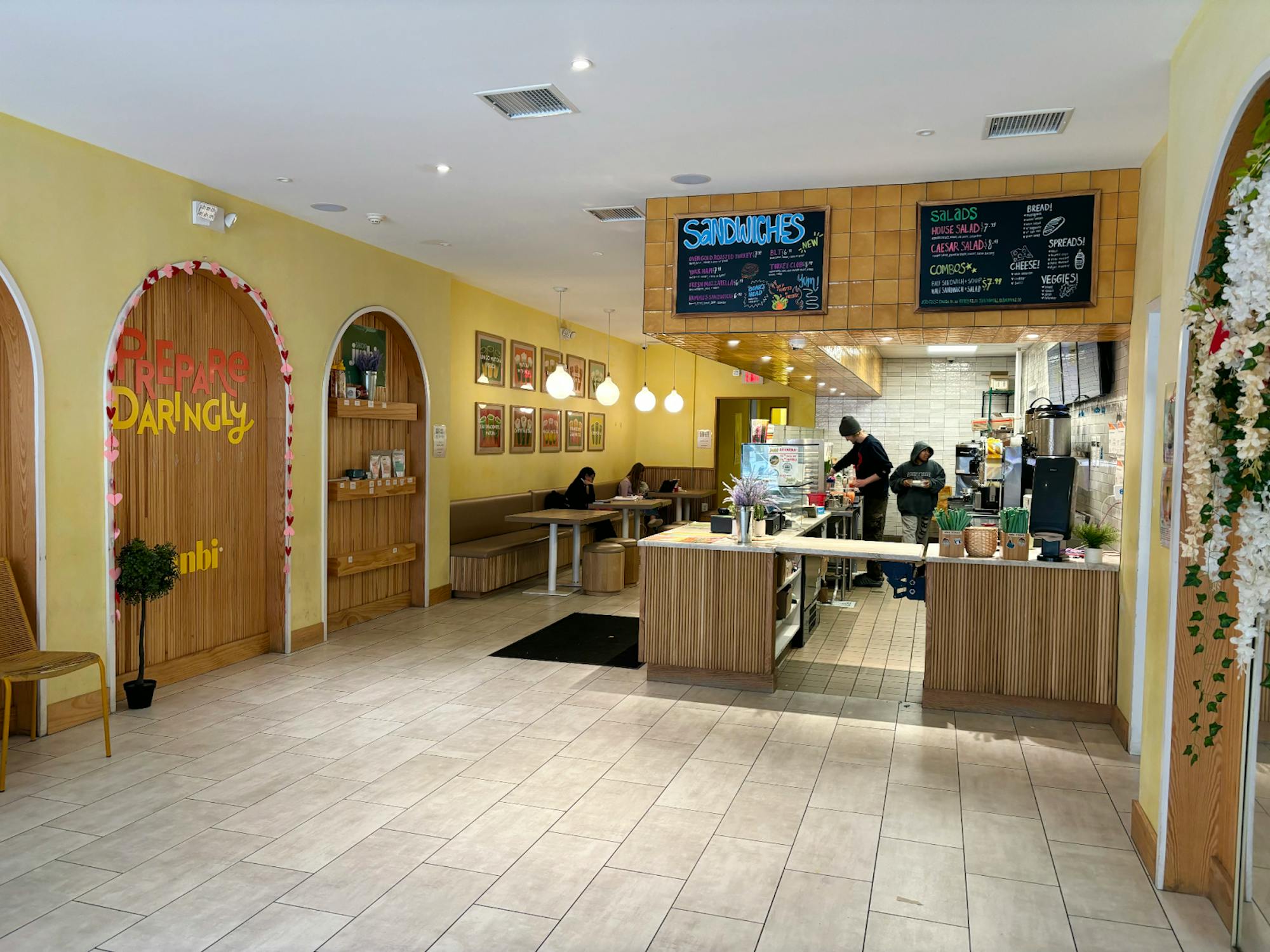 An ordering area, pick-up counter, and seating for customers clustered together towards the back of a cafe.