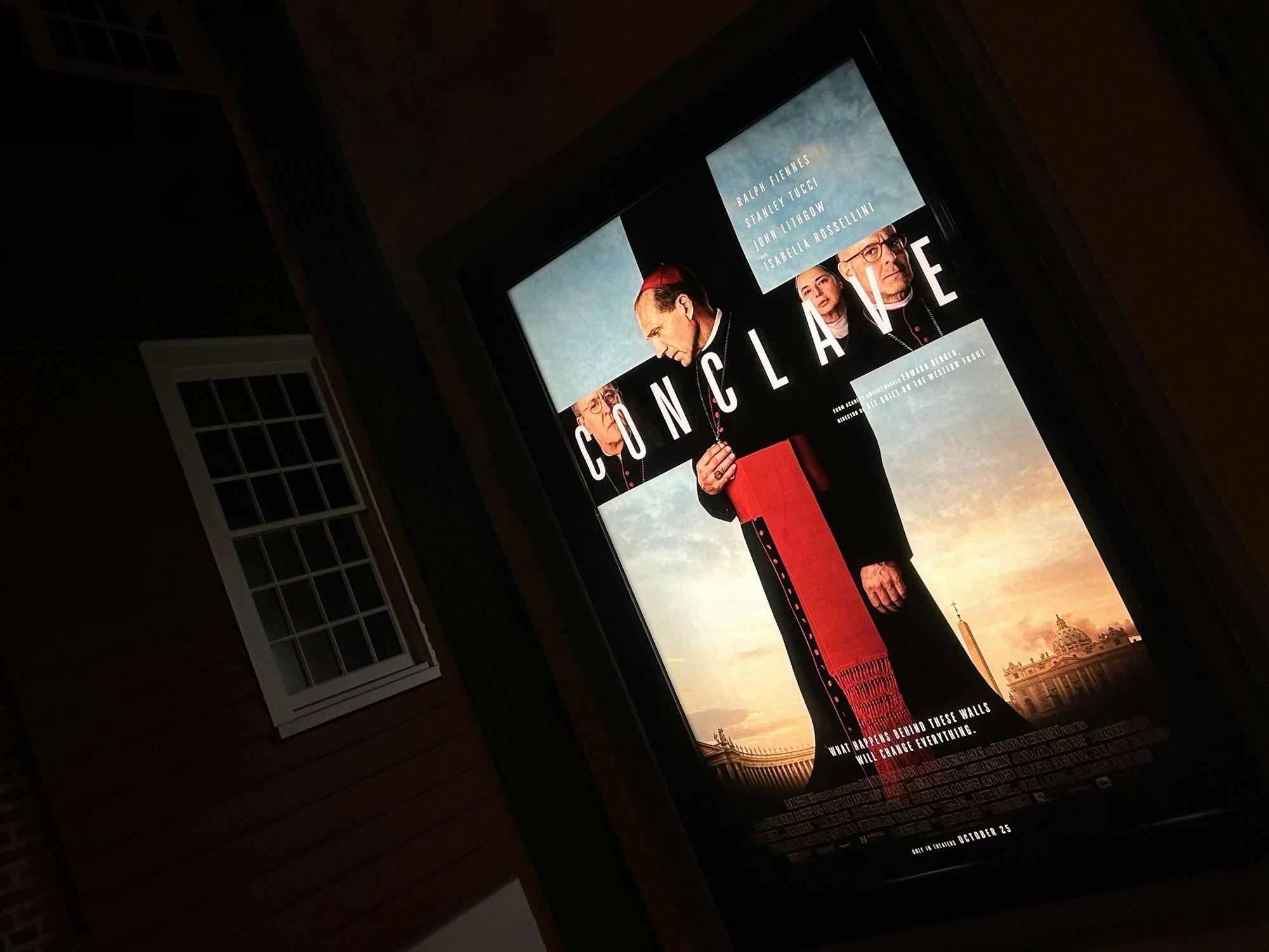 A brightly-lit movie poster of a pope in a black gown and a red mitre. 