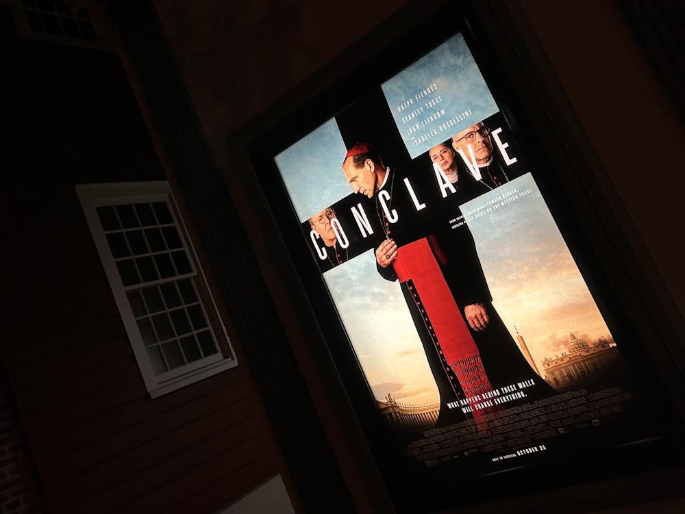 A brightly-lit movie poster of a pope in a black gown and a red mitre. 