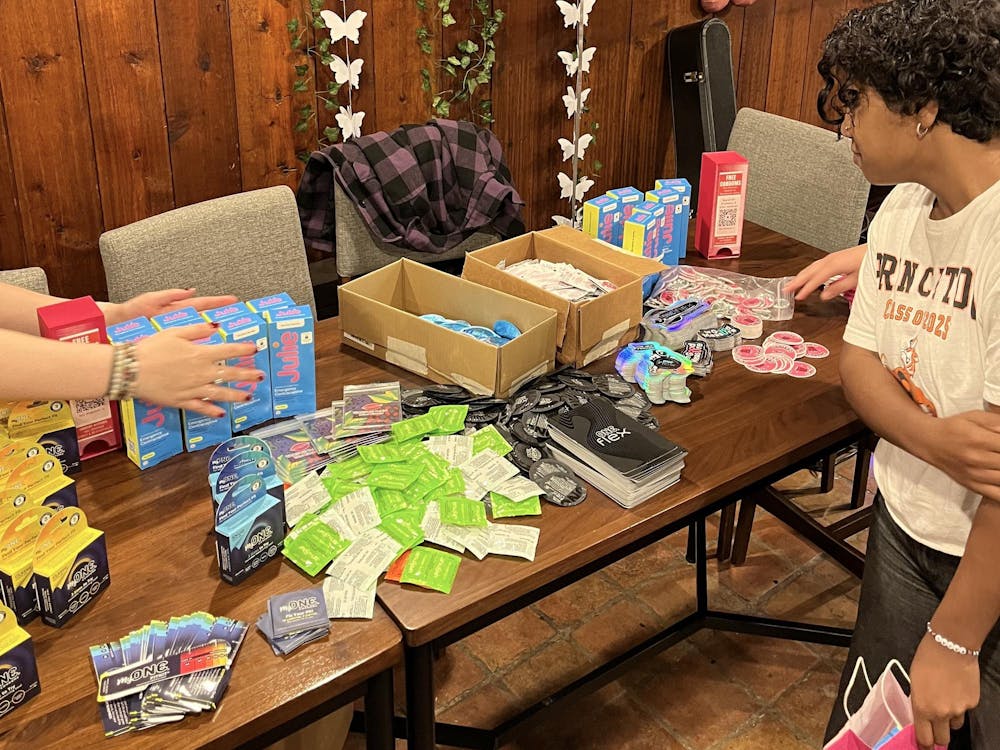 A rectangular table displays condoms from several condom brands and stickers. A student looks over the table while a hand behind them reaches for a sticker.