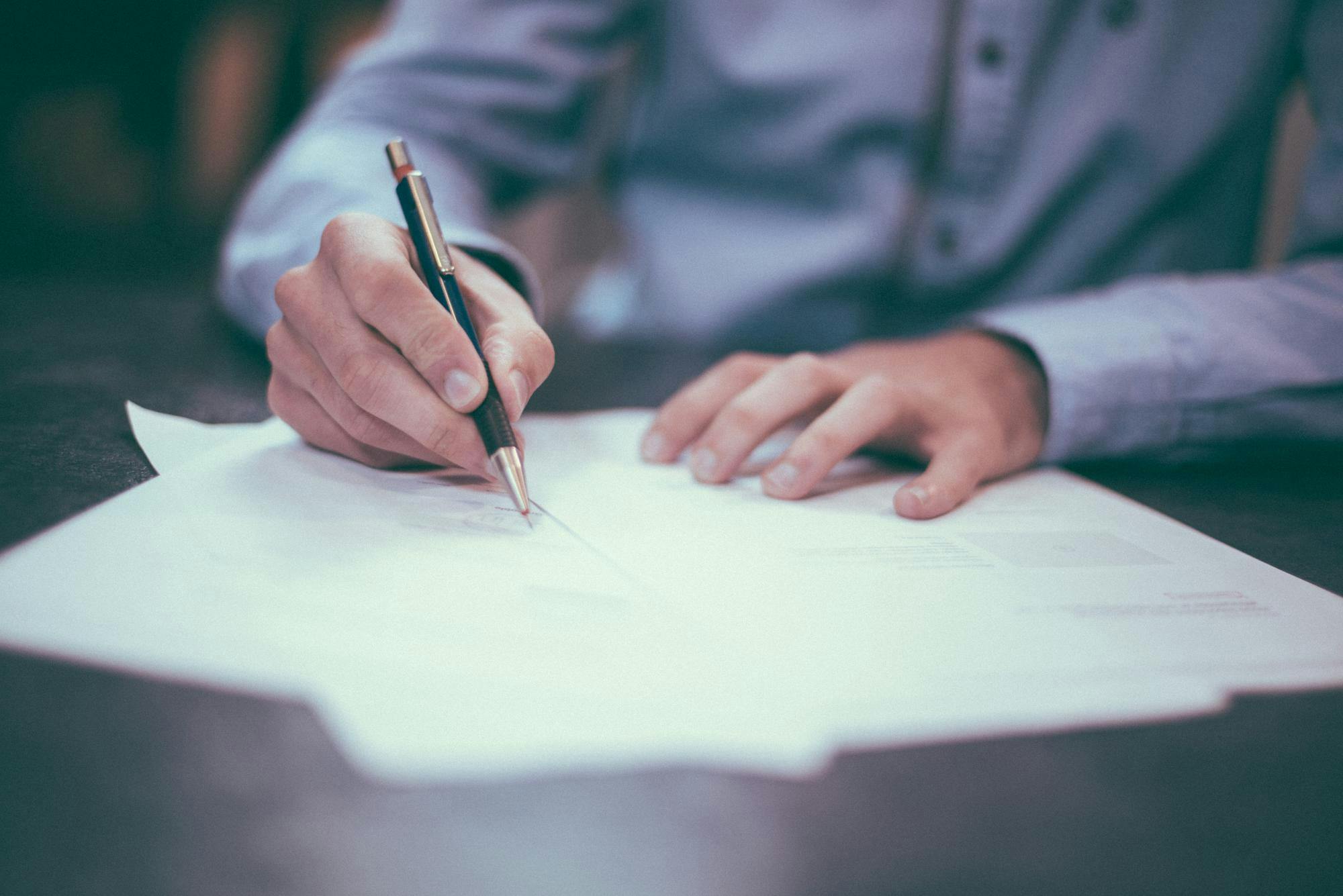 Man with black and gold pen signing stack of papers
