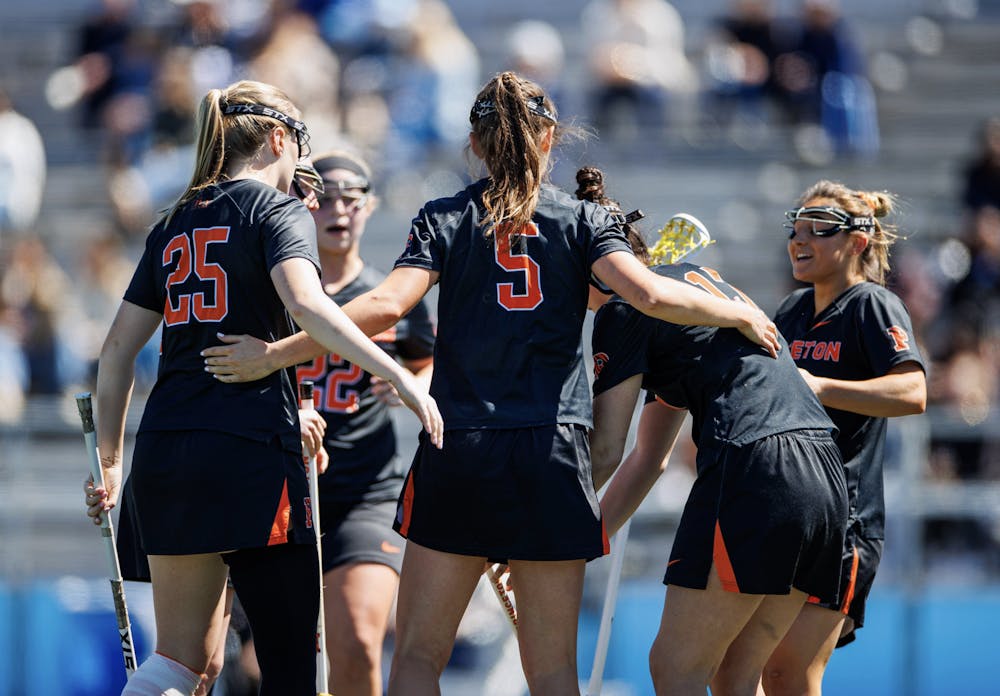 A group of players in a huddle with black jerseys on and holding lacrosse sticks.