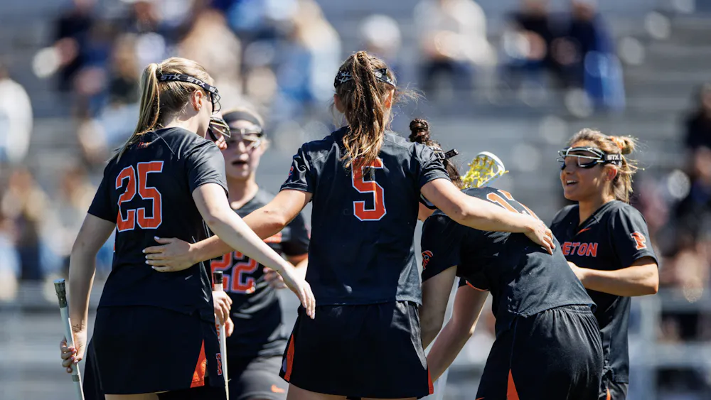 A group of players in a huddle with black jerseys on and holding lacrosse sticks.
