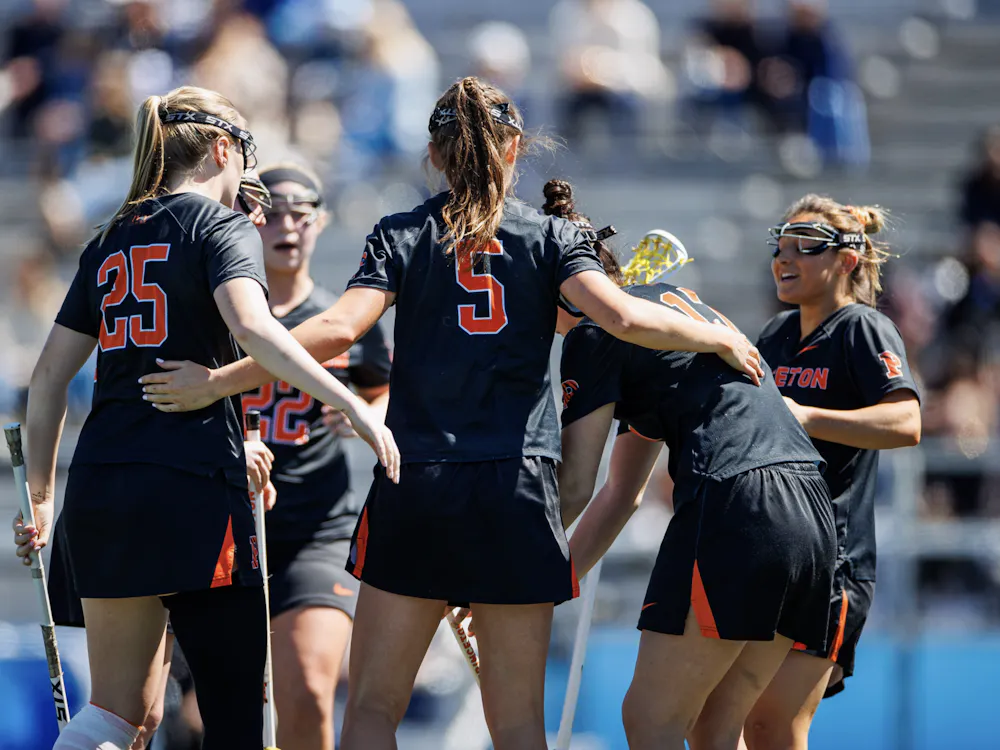 A group of players in a huddle with black jerseys on and holding lacrosse sticks.