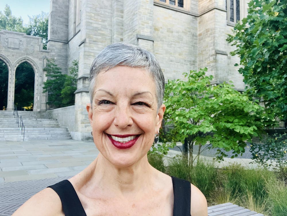 A woman with short gray hair smiles at the camera. Stone arches stand behind her.