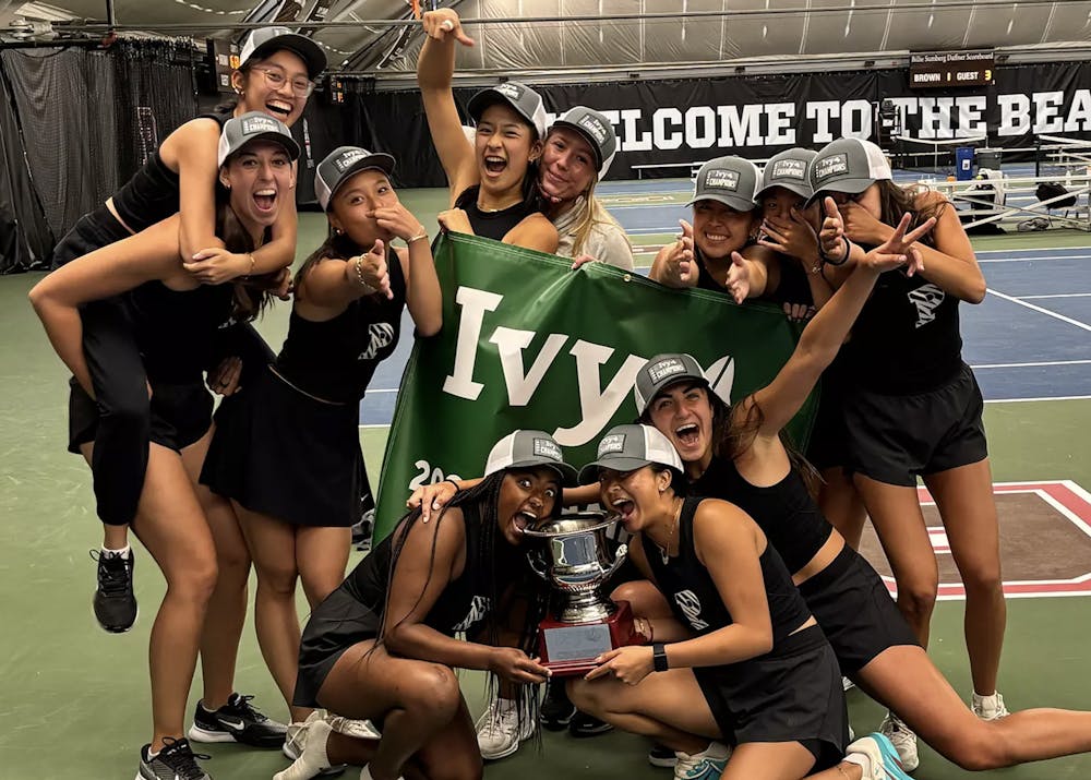 Princeton tennis athletes in black jerseys celebrating and holding a trophy