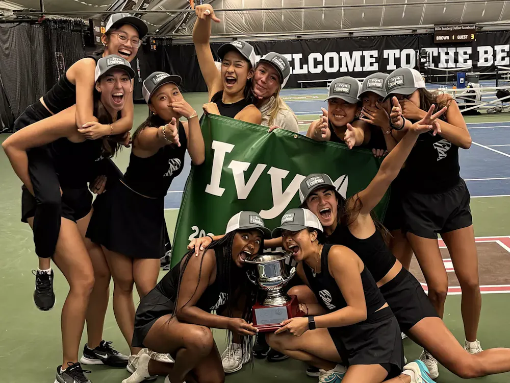 Princeton tennis athletes in black jerseys celebrating and holding a trophy