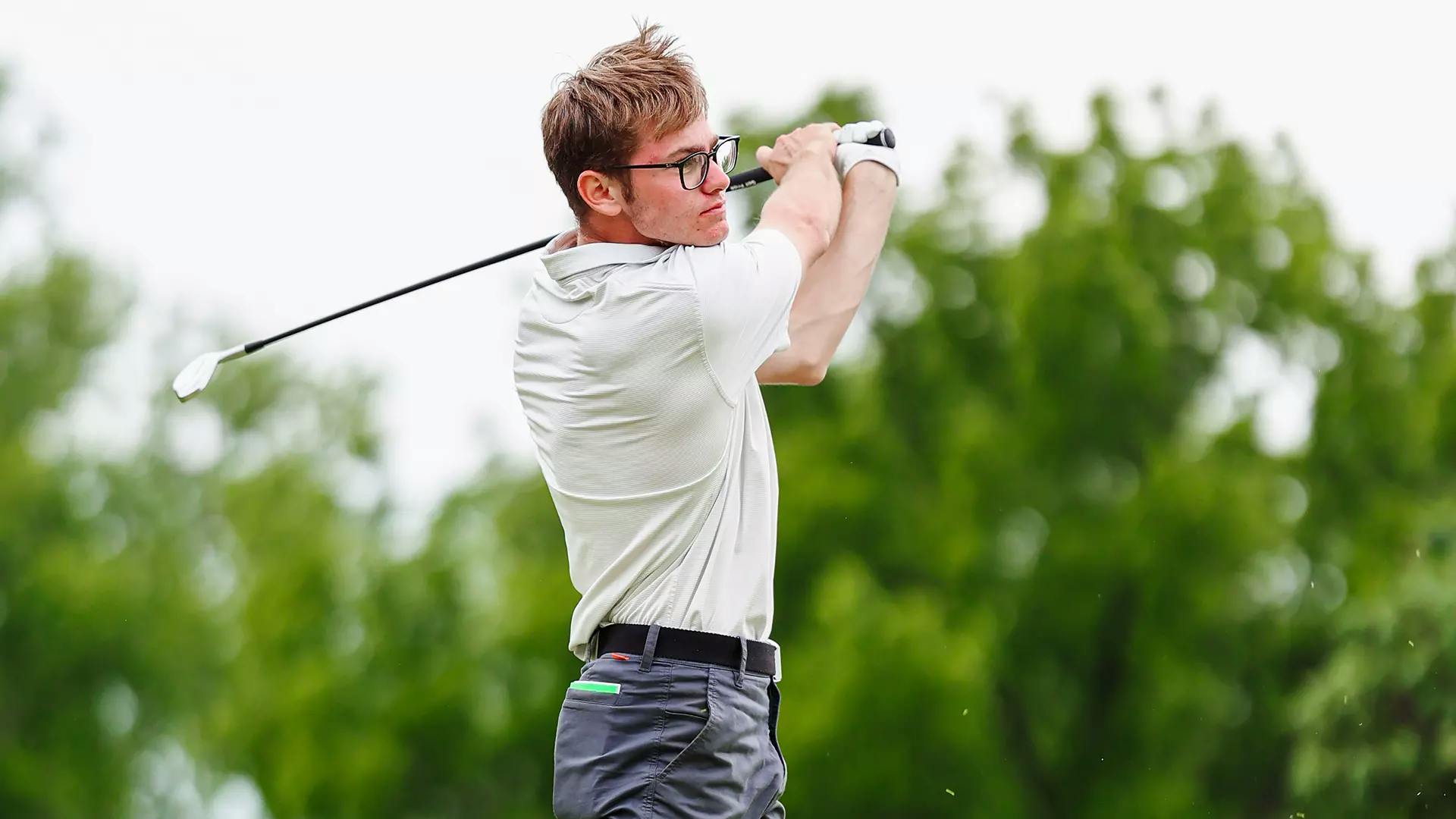 Man in white polo shirt follows through on golf swing.