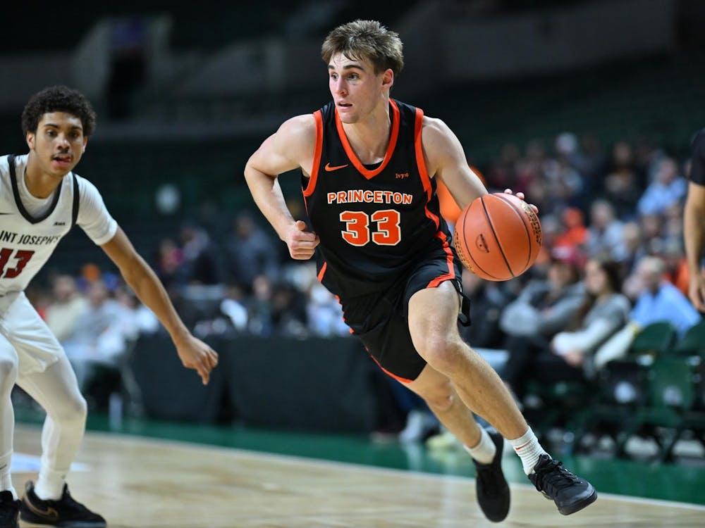 A Princeton men’s basketball player drives toward the basket during a game against Saint Joseph’s, dribbling with his right hand as a defender closes in and a referee watches from the baseline.