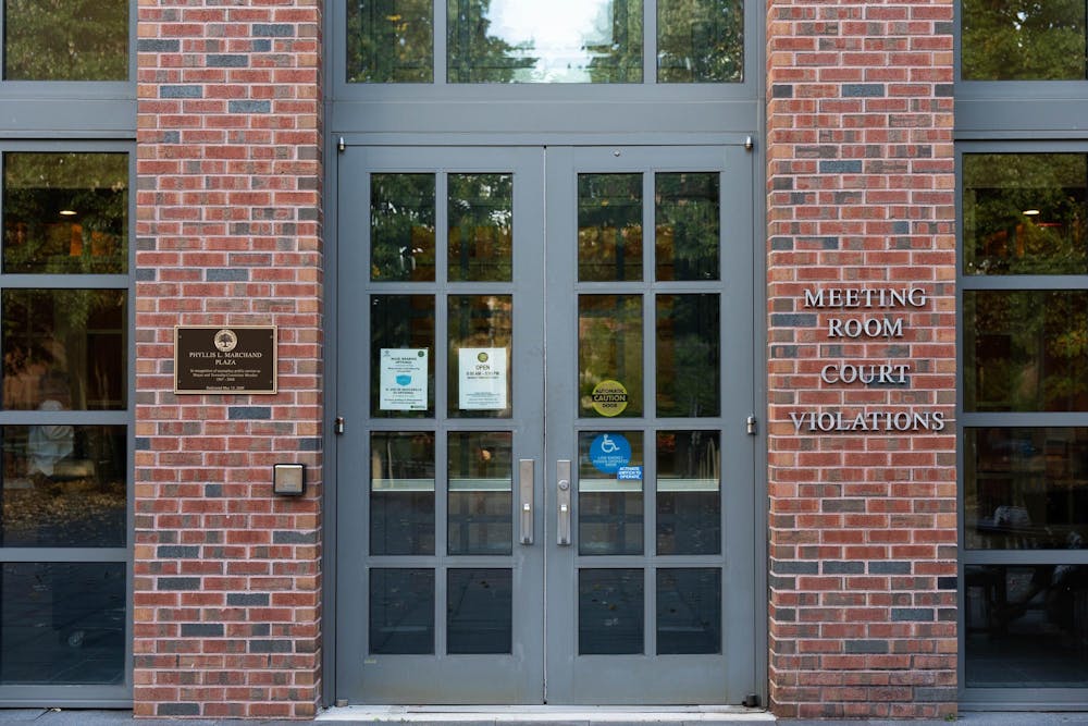 A glass-paned door is at the center of the exterior of a brick building. A sign on the building reads, “Meeting Room Court Violations.”