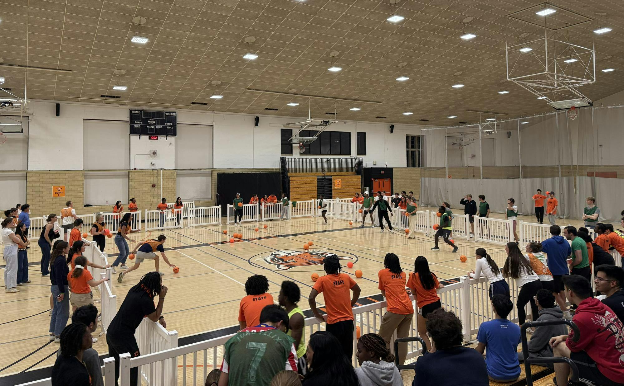 Dozens of people inside a gymnasium with several orange balls spread across the floor.