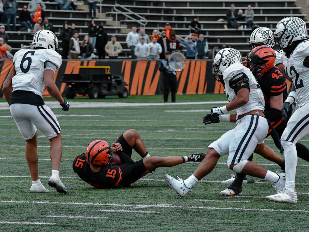 Princeton player in black and orange uniform down on the football field with Yale players surrounding him. 