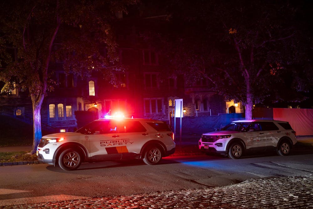 Two Public Safety cars parked on a street curb with their overhead lights flashing blue and red.