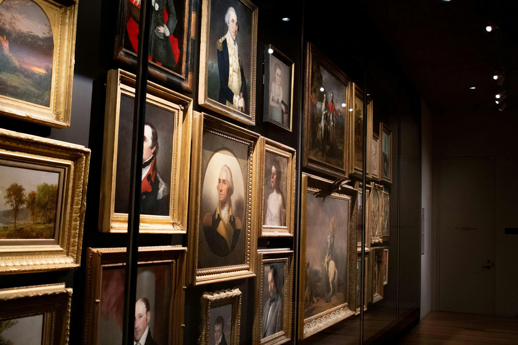 An array of portraits are against a wall behind a glass case.