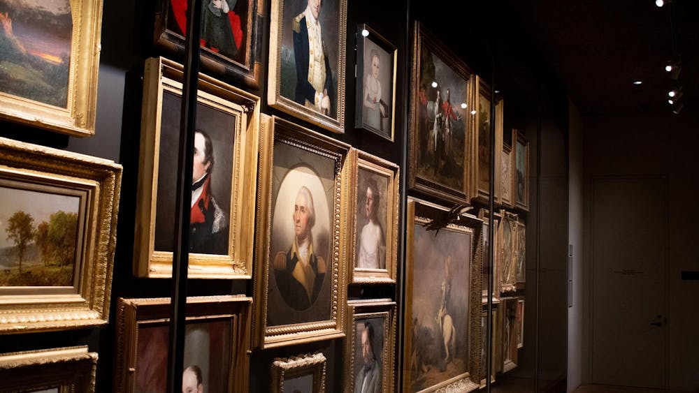 An array of portraits are against a wall behind a glass case.