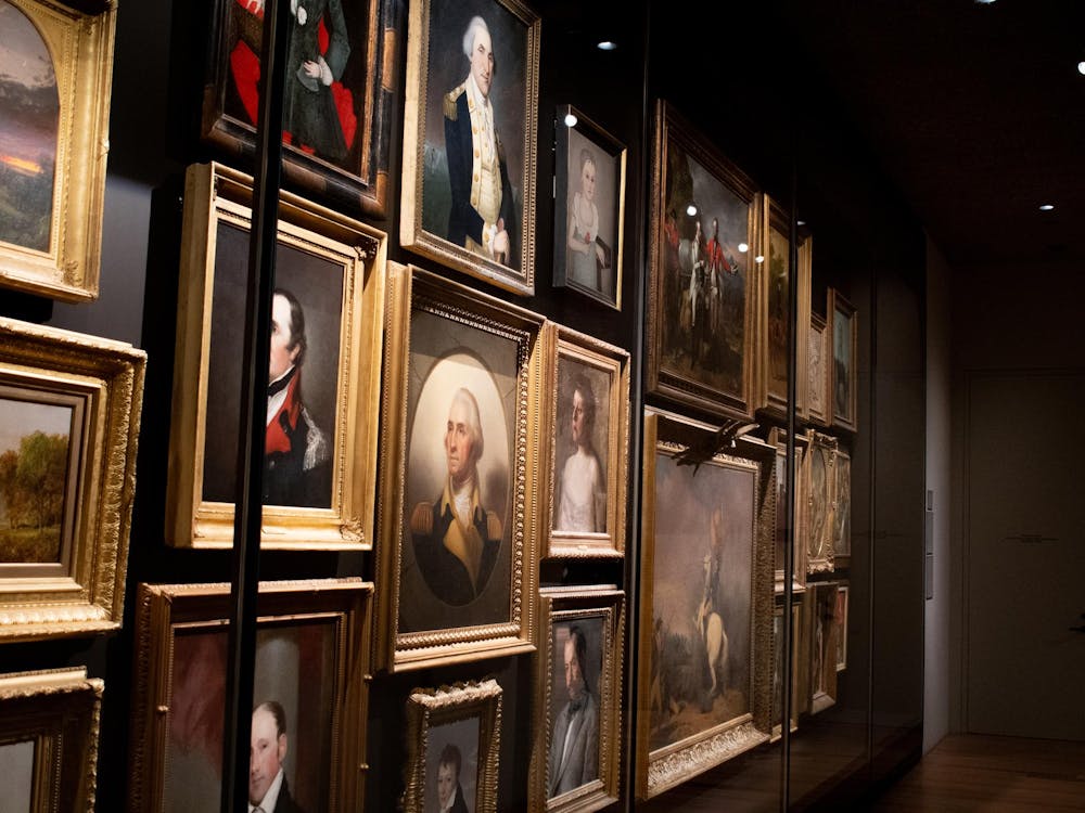 An array of portraits are against a wall behind a glass case.