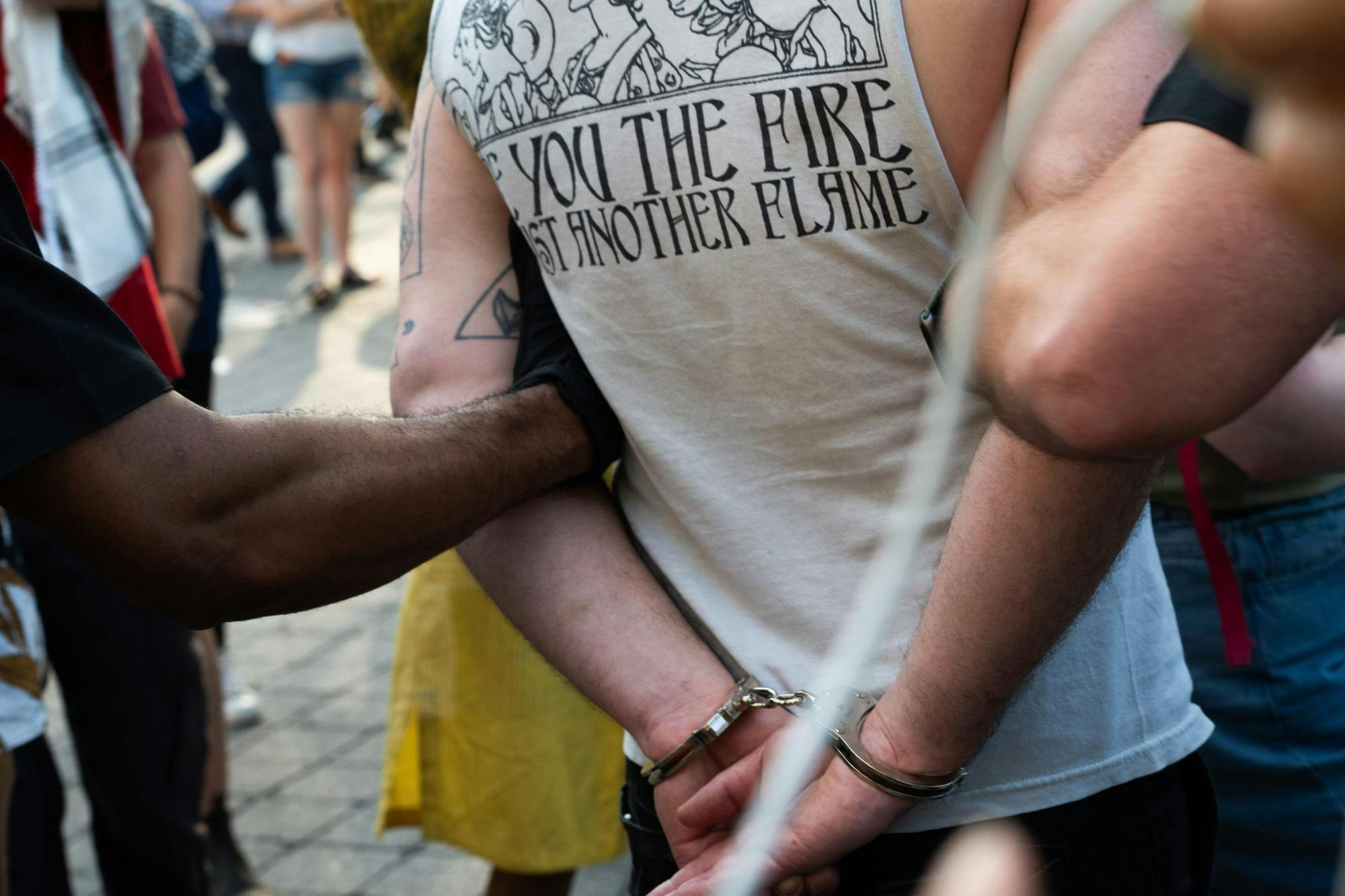 A handcuffed man’s arms are held behind his back as he is led through a crowd. 