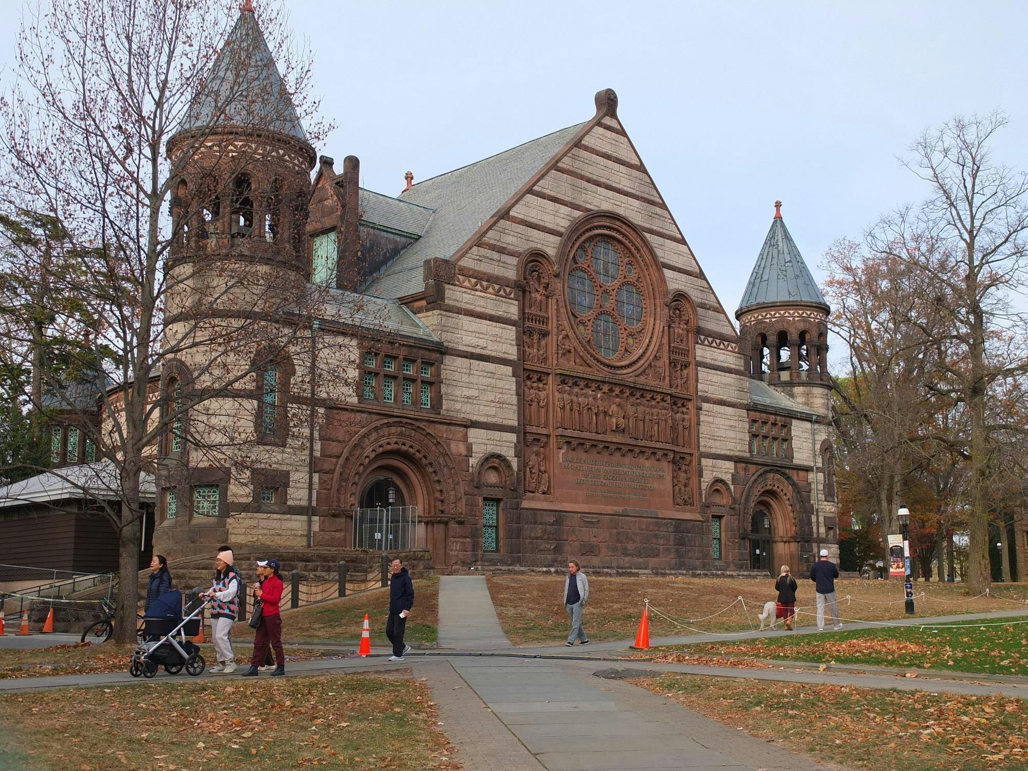A large building with brown and white paneling. People are walking along a path in front of the building.