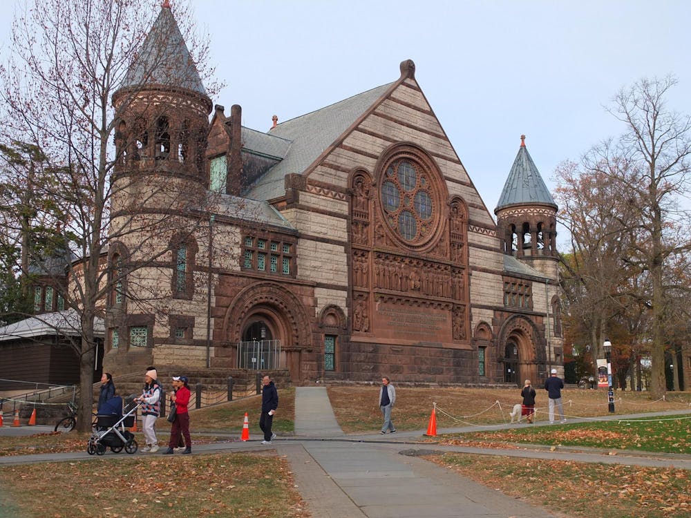 A large building with brown and white paneling. People are walking along a path in front of the building.