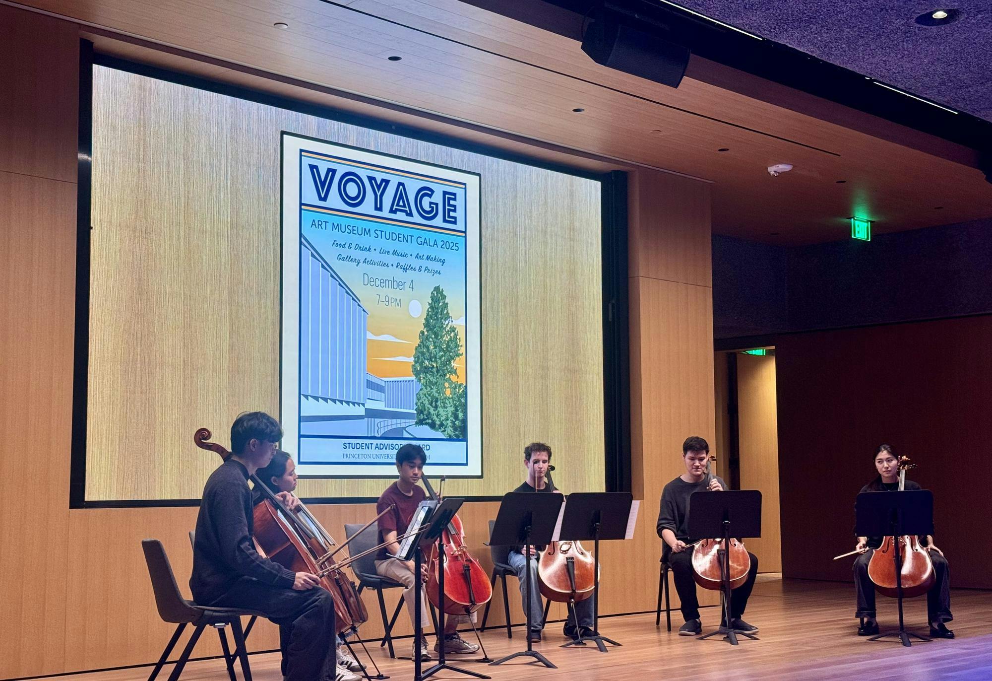 Six students sitting on chairs in a semi-circle, holding cellos, looking at music stands.