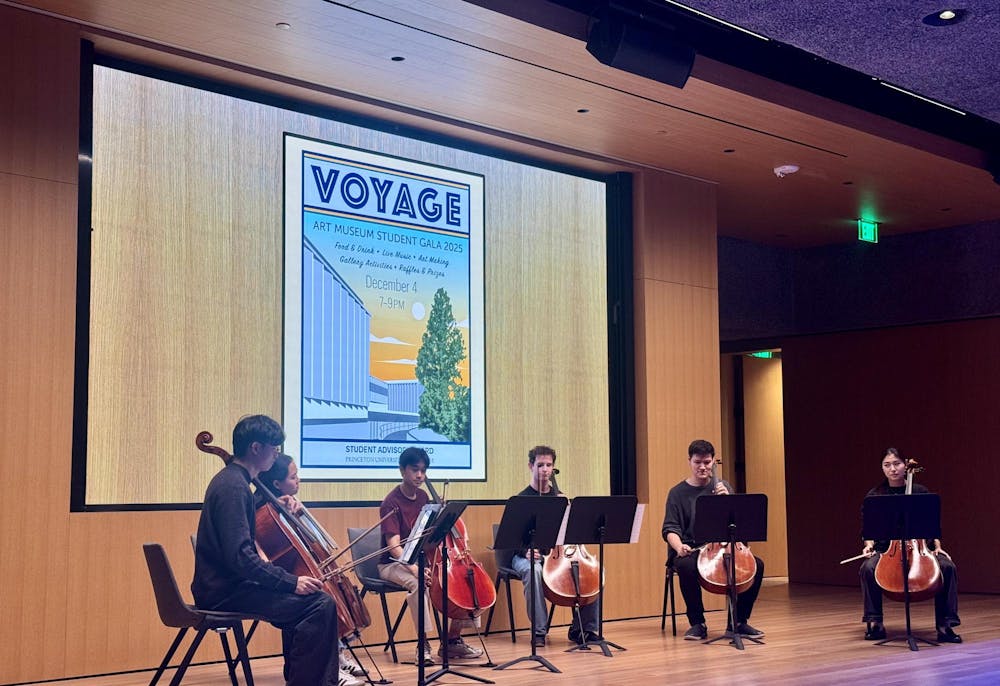 Six students sitting on chairs in a semi-circle, holding cellos, looking at music stands.