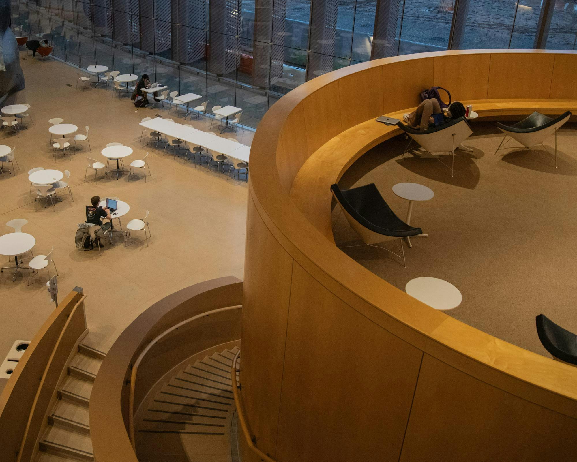 Student studying in circular space; students studying on level directly below in an interior cafe. 