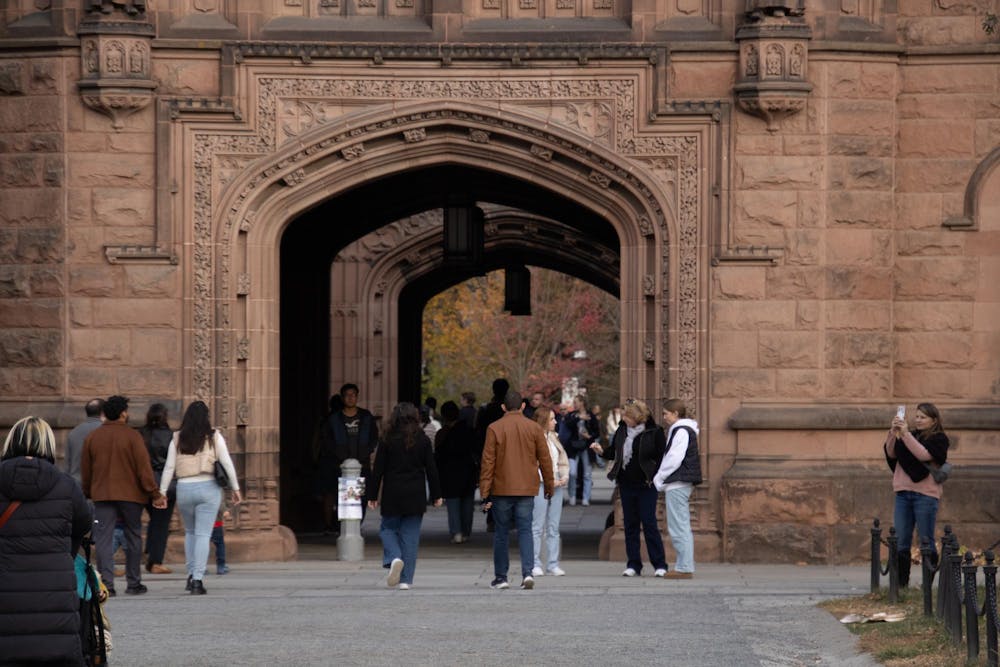 A ground shot of an arch entrance, of a reddish stone building. People are walking around and through the building.