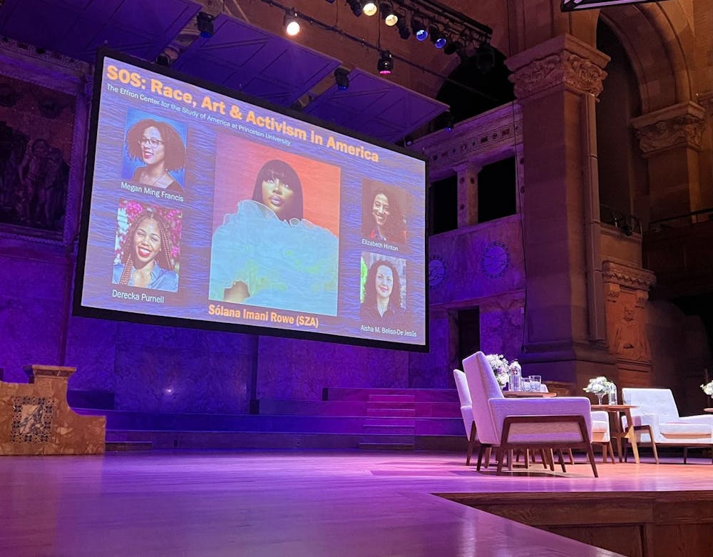 Behind a set of chairs, a screen displays portraits of participants in an academic discussion.