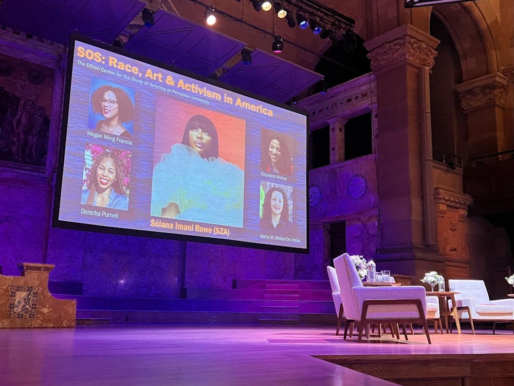 Behind a set of chairs, a screen displays portraits of participants in an academic discussion.