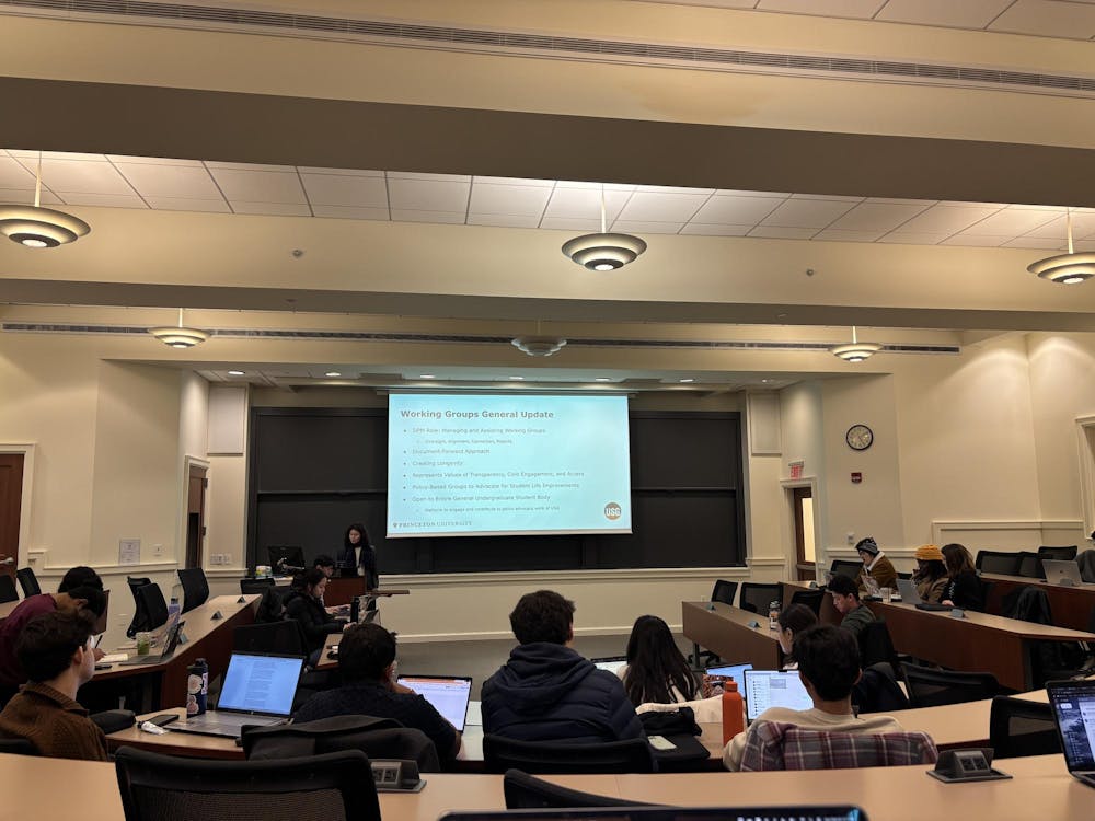 A screen reads Working Groups General Update. People are sat in a horseshoe shape around the screen. The backs of several people's heads can be seen.