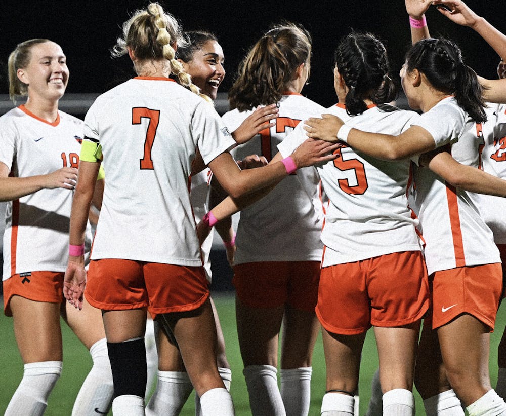 A group of women in orange and white soccer kits smiling and celebrating on a field. 