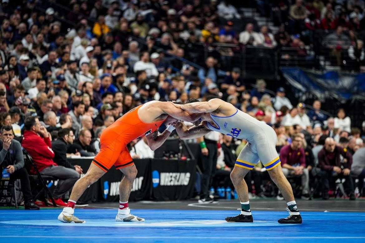 Man in orange wrestling uniform wrestles against man in gray uniform