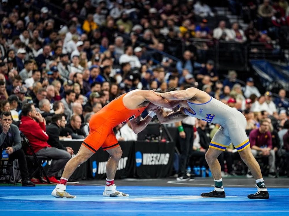 Man in orange wrestling uniform wrestles against man in gray uniform