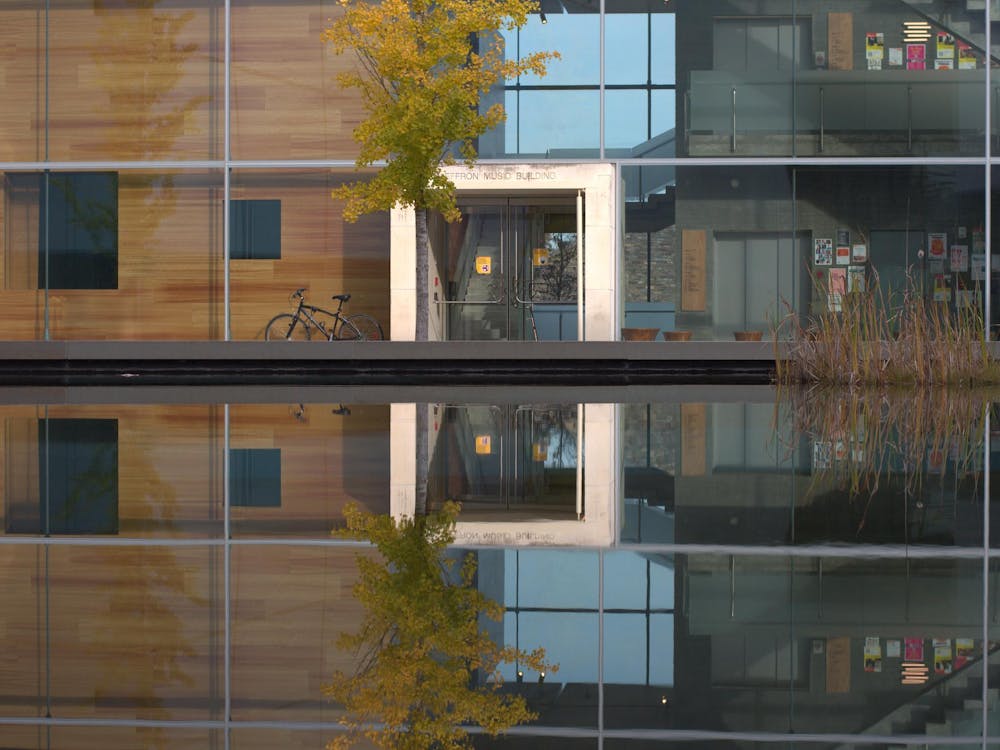 A tree and glass building reflect over a pond of water.