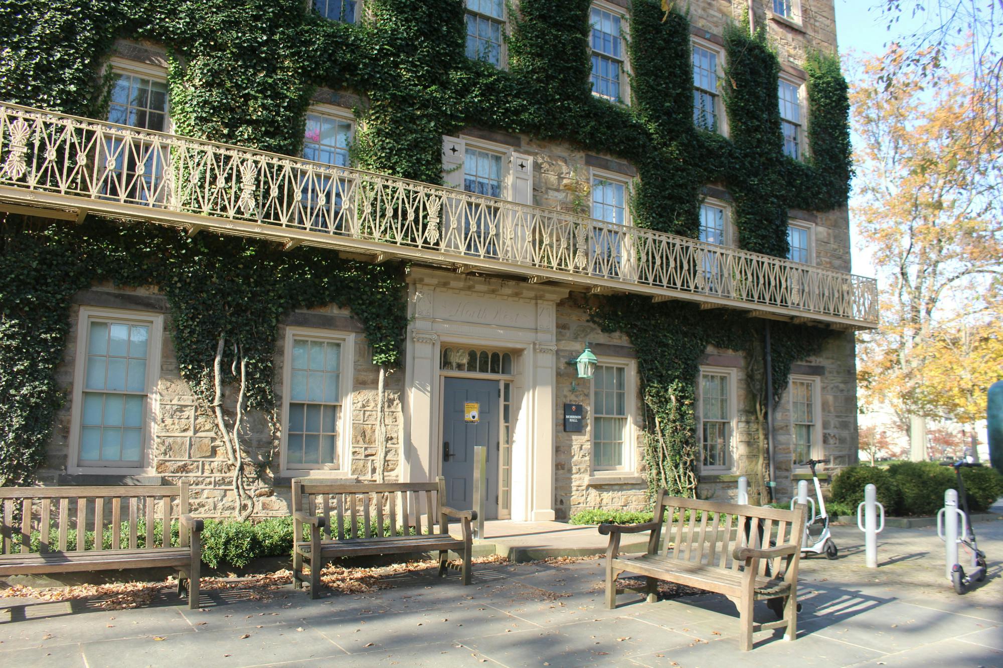 A building covered in ivy with three benches in front of it.