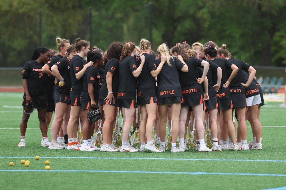Women’s lacrosse team in center of field, huddled with their backs towards the camera.