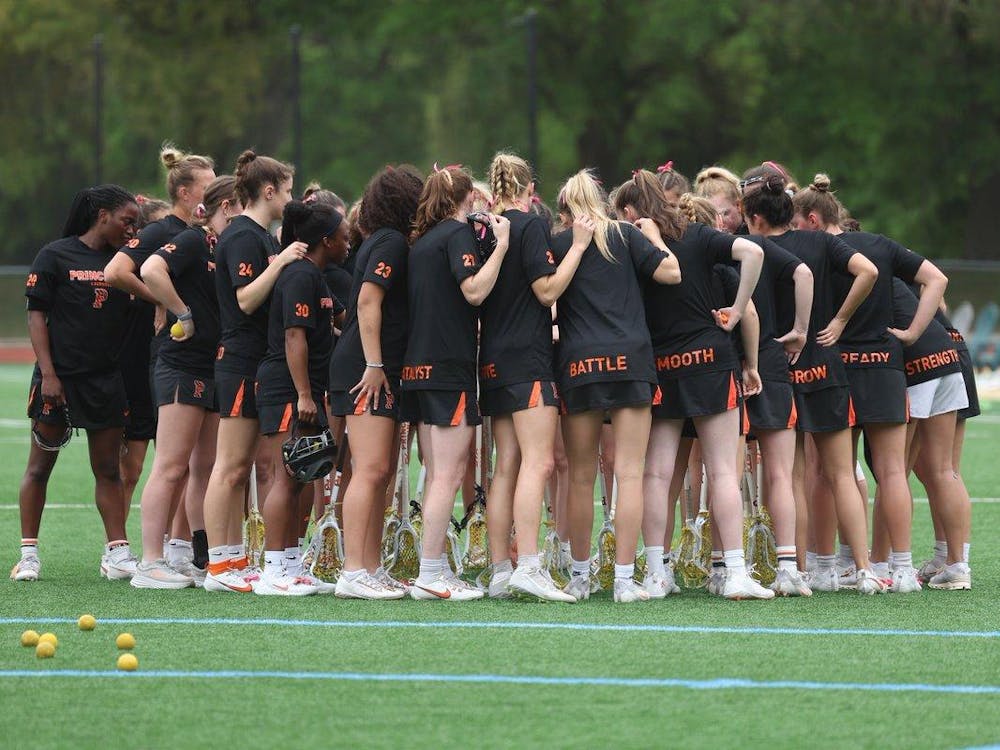 Women’s lacrosse team in center of field, huddled with their backs towards the camera.