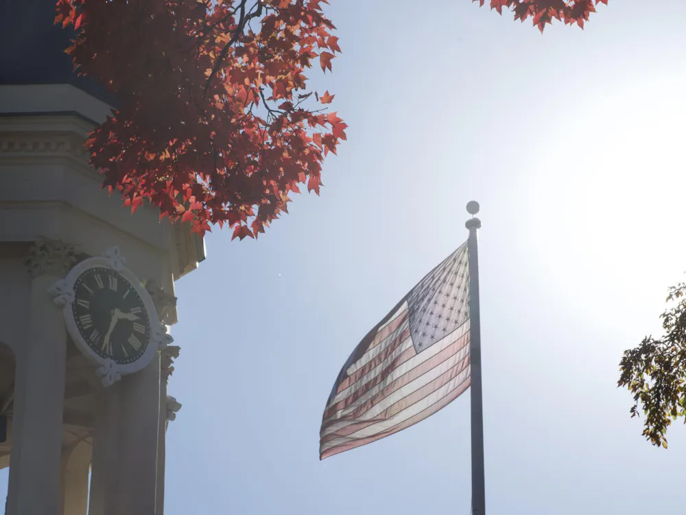 La bandera estadounidense ondea en un día soleado junto a un campanario de color beige.
