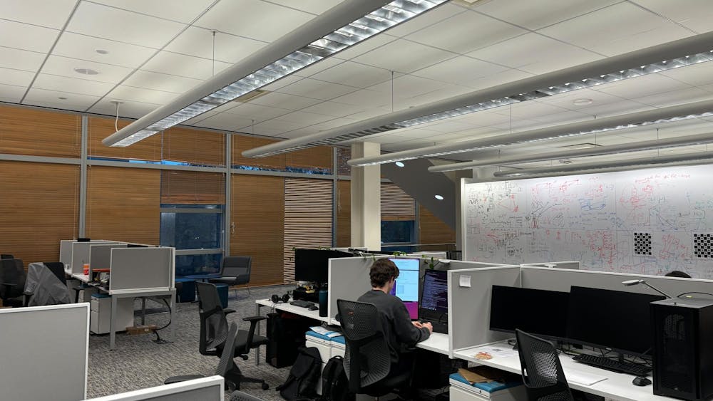 Gray cubicles with computers are lined up in rows in a basement room.