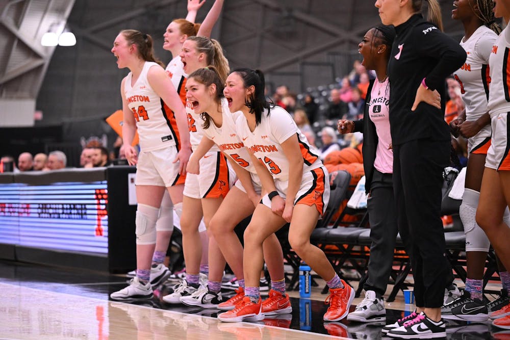 Women in white basketball jerseys cheering on their teammates from the curtsied bench.