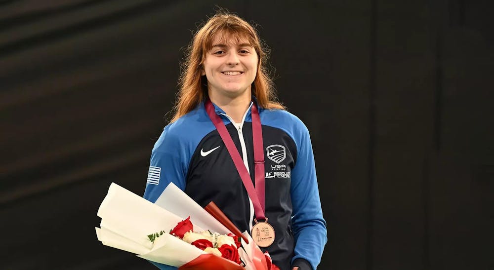 A woman standing with a medal around her neck holding flowers and smiling 
