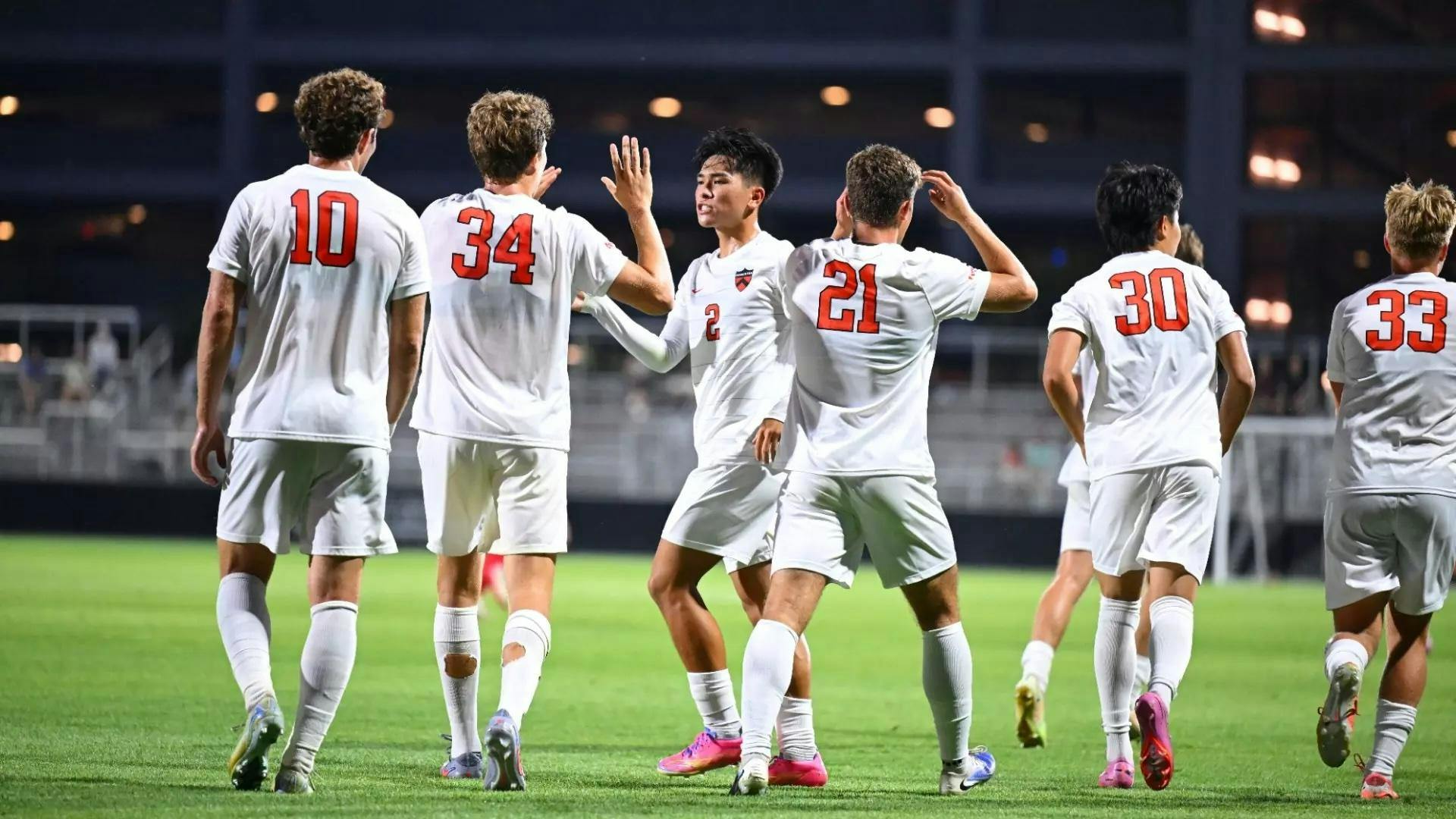 Soccer players in white uniforms high five each other on a green turf field.
