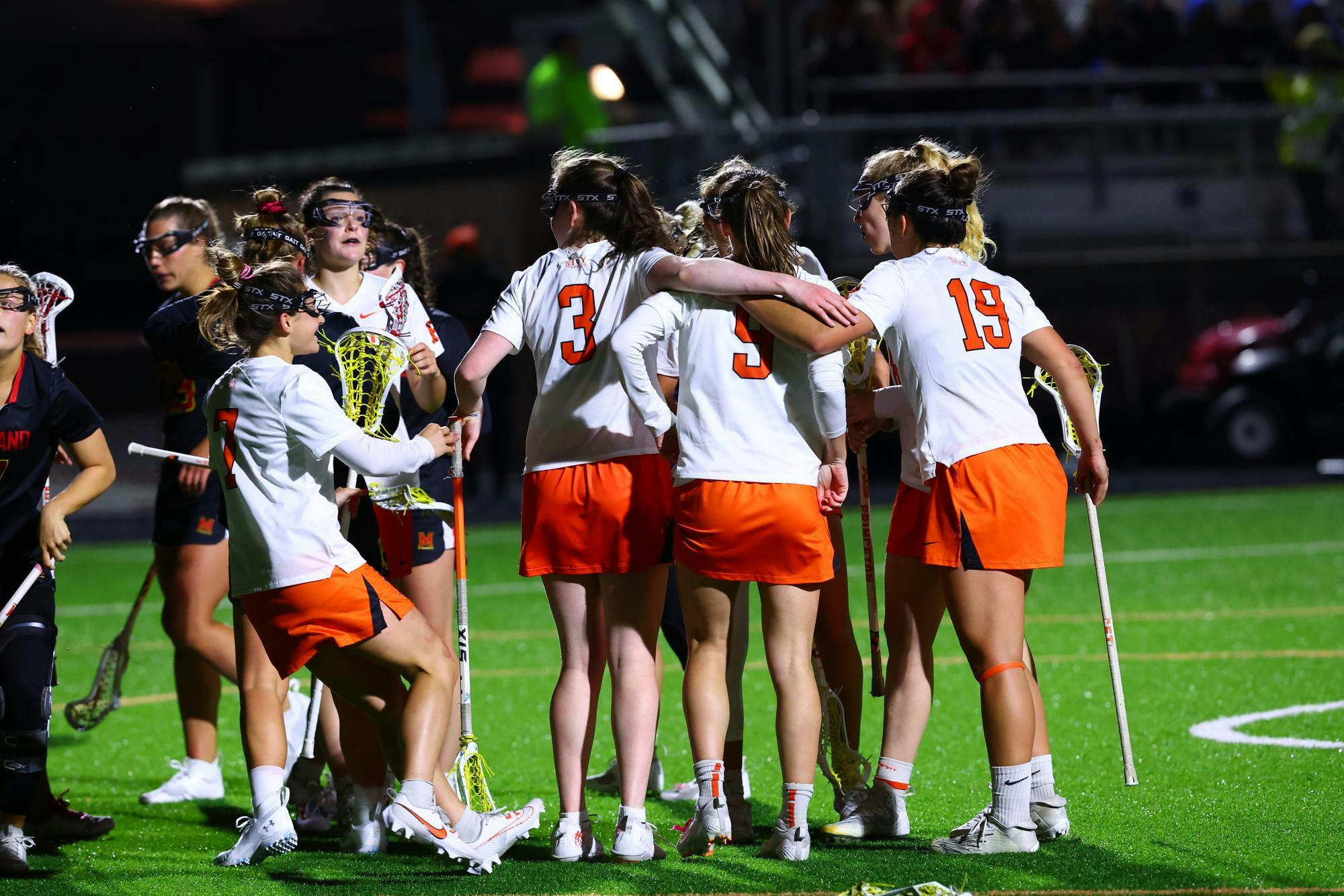 Group of people in white shirts huddled together on green grass.
