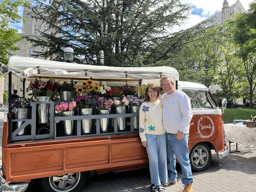 A couple stands in front of a muted orange pick up truck filled with flowers. 