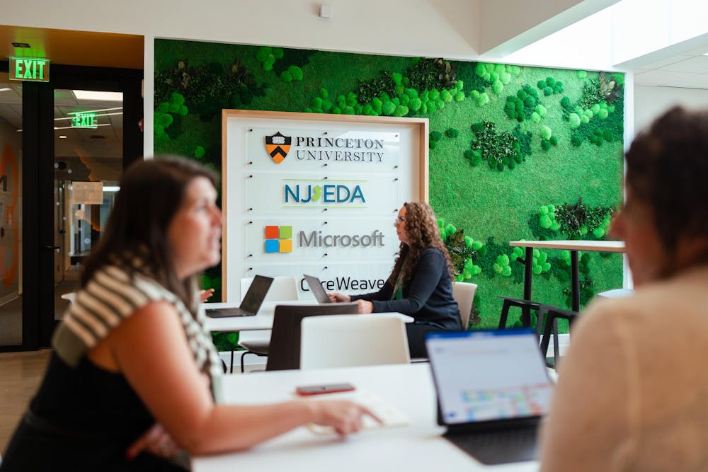 Focused on a woman working on her computer, sitting in front of the AI Hub Founding Partners sign. 